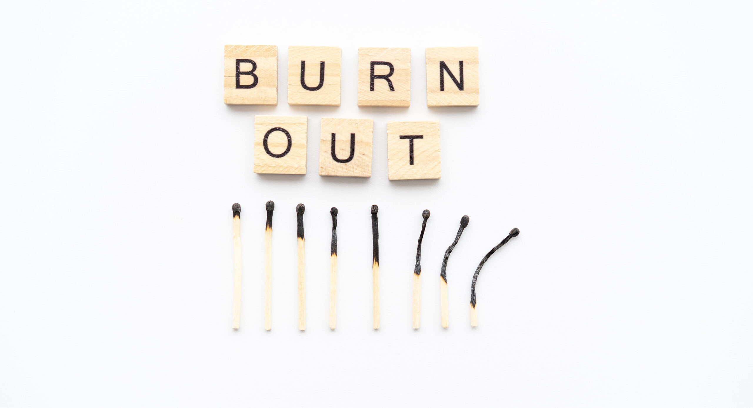 Scrabble-style wooden tiles spell out "BURN OUT" on a white background, positioned above a row of burnt matches that progressively become more charred and bent.