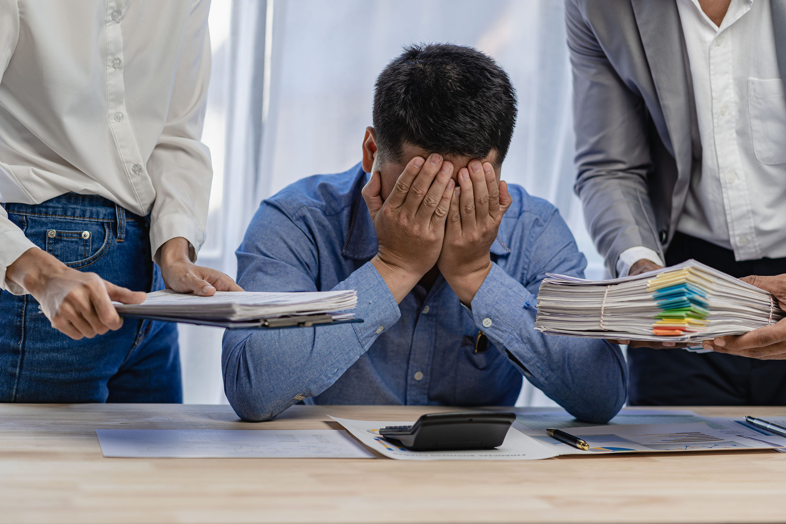 Asian male employee is stressed with paperwork and holding his head with many friends handing over work. concept of work